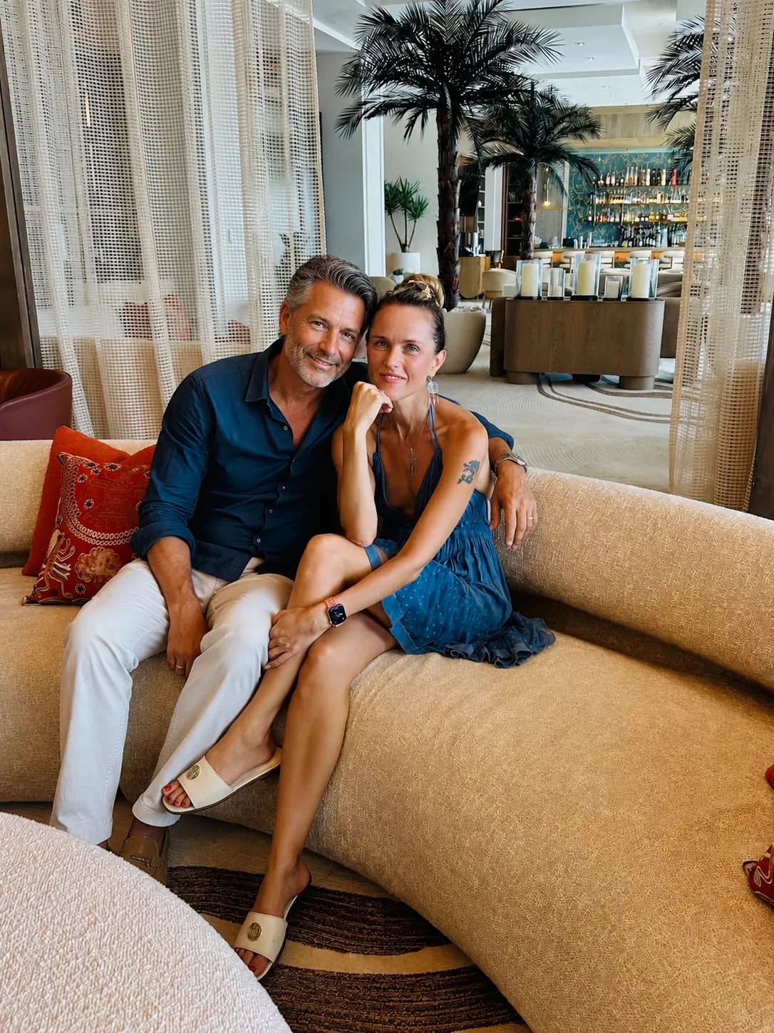 Maria and her partner smiling together on a lounge sofa